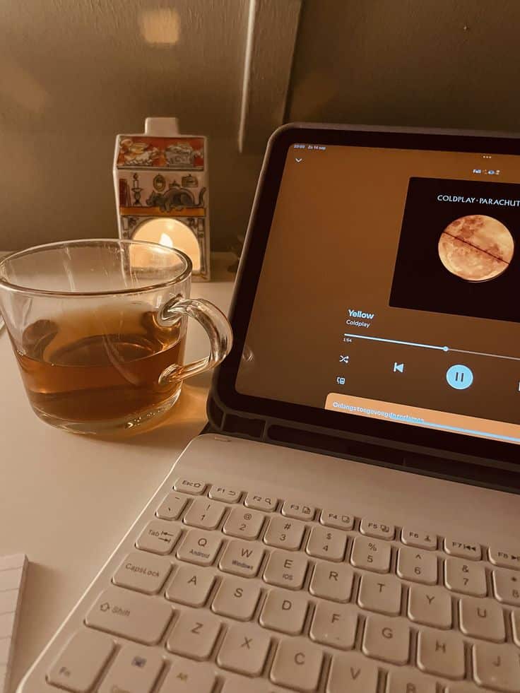 Cozy setup with a tablet playing music, a cup of tea, and a glowing lamp on a desk, perfect for a relaxing evening.