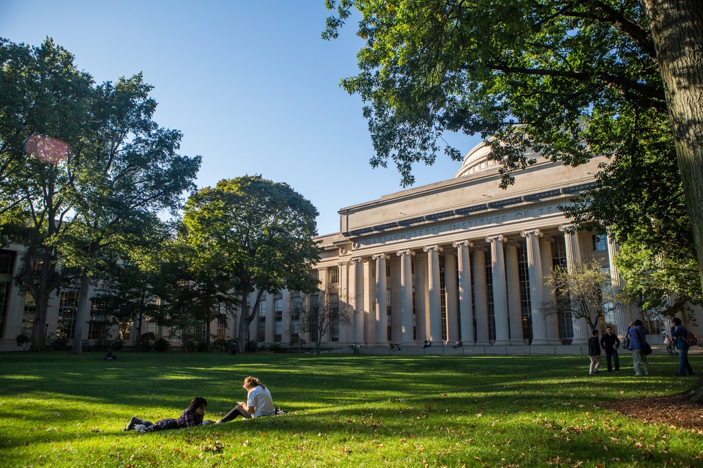 01 Students relax on a sunny lawn in front of a grand, columned university building surrounded by trees. | Sky Rye Design Students relax on a sunny lawn in front of a grand, columned university building surrounded by trees.