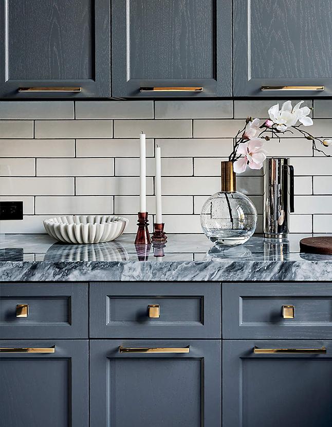 Modern kitchen with gray cabinetry, marble countertop, white subway tile backsplash, floral vase, candles, and decorative bowl.