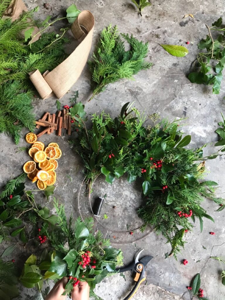 054df02fb2588dafd54f669ed54d58cc Handcrafting a festive wreath with greenery, dried oranges, cinnamon sticks, and berries on a concrete surface. | Sky Rye Design Handcrafting a festive wreath with greenery, dried oranges, cinnamon sticks, and berries on a concrete surface.