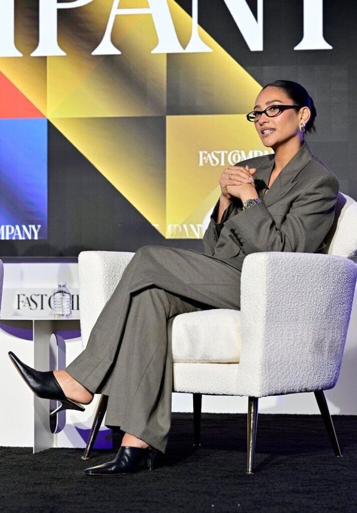 Businesswoman in a gray suit sits on a white chair during a panel discussion at a Fast Company event, engaging and focused.