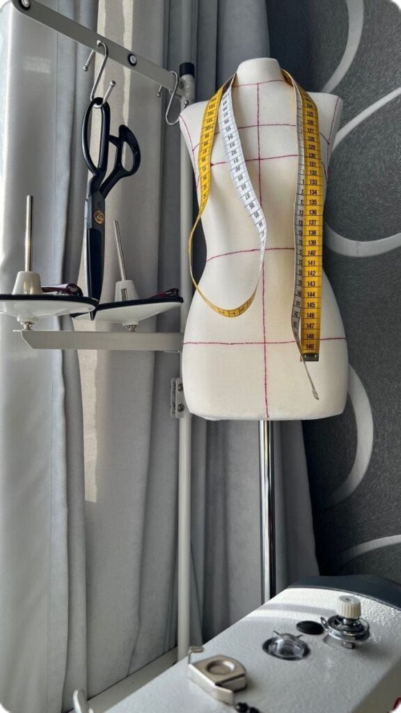 _ 1 Sewing mannequin with measuring tape, scissors, and tools beside window, highlighting a tailored fashion workspace. | Sky Rye Design Sewing mannequin with measuring tape, scissors, and tools beside window, highlighting a tailored fashion workspace.