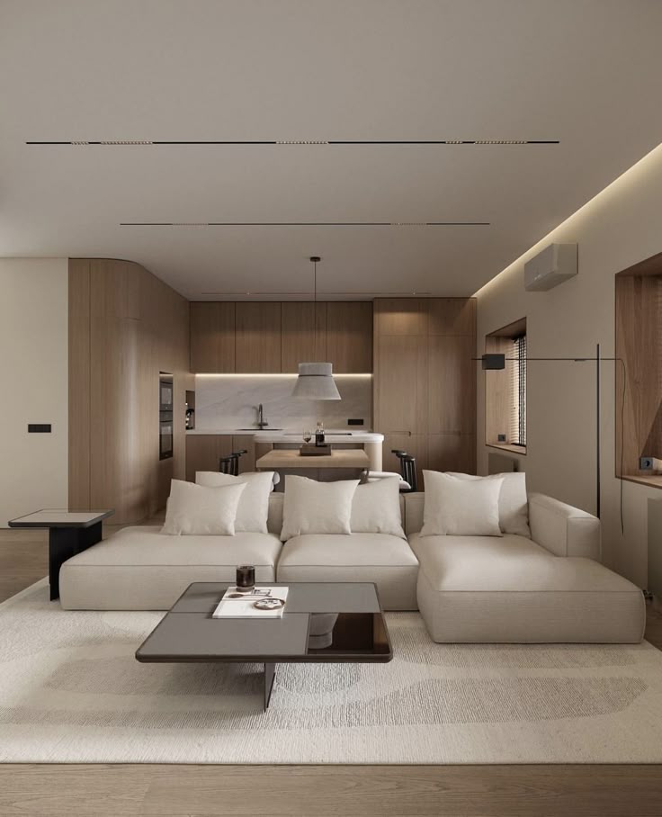 Screenshot Modern open-concept living room with beige sectional sofa, stylish coffee table, and minimalist wooden kitchen in background. | Sky Rye Design Modern open-concept living room with beige sectional sofa, stylish coffee table, and minimalist wooden kitchen in background.