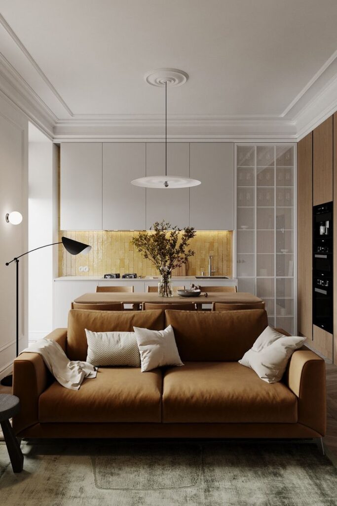 Modern kitchen and living area with brown sofa, minimalist decor, white cabinets, and natural wood accents. Cozy, contemporary design.