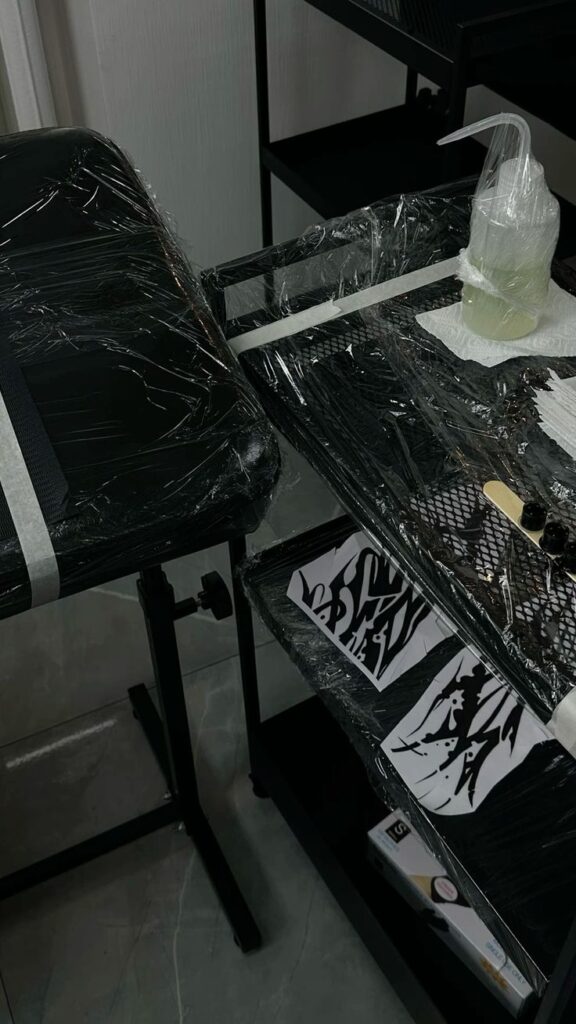 _ 1 Tattoo studio setup with sanitized equipment and ink trays, ready for clients. Hygienic workspace with plastic wrap covering surfaces. | Sky Rye Design Tattoo studio setup with sanitized equipment and ink trays, ready for clients. Hygienic workspace with plastic wrap covering surfaces.