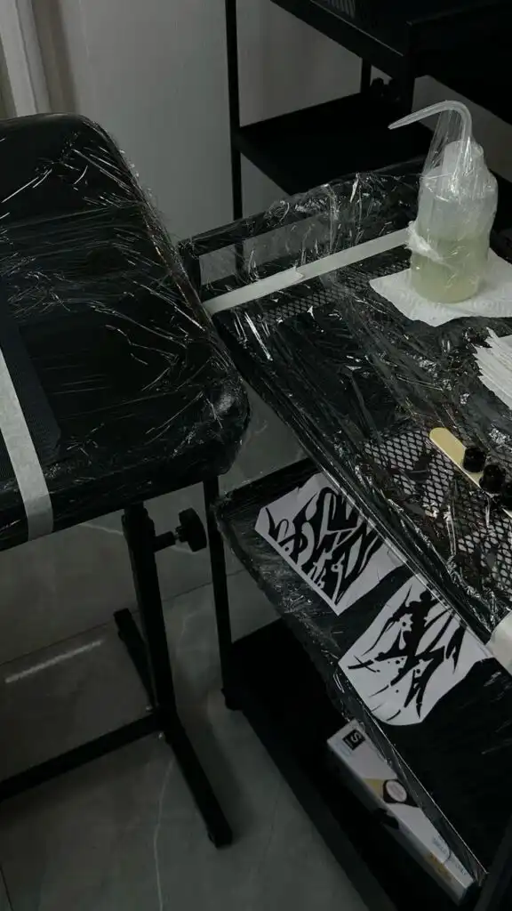 Tattoo studio setup with sanitized equipment and ink trays, ready for clients. Hygienic workspace with plastic wrap covering surfaces.
