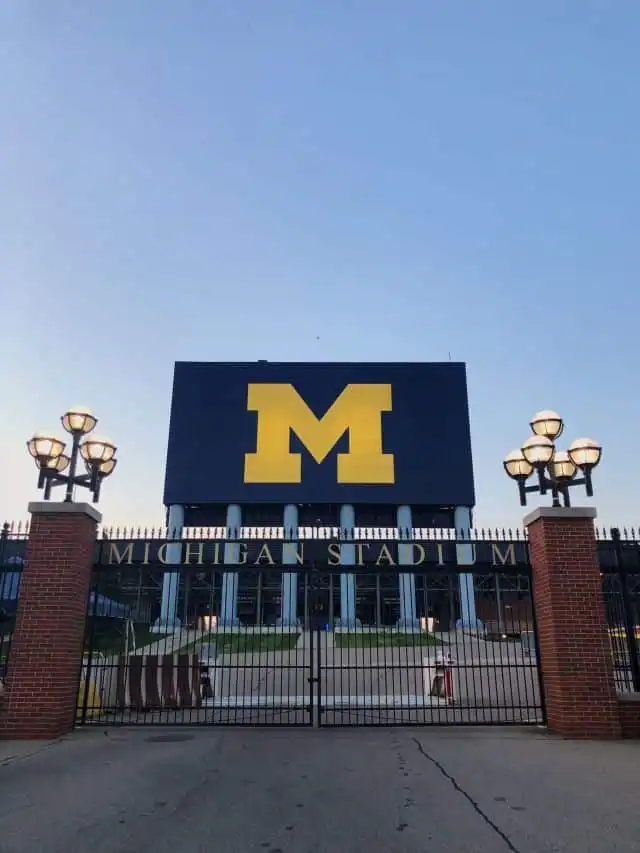Michigan Stadium entrance with large block M sign under a clear sky at sunset, showcasing iconic sports venue and architecture.