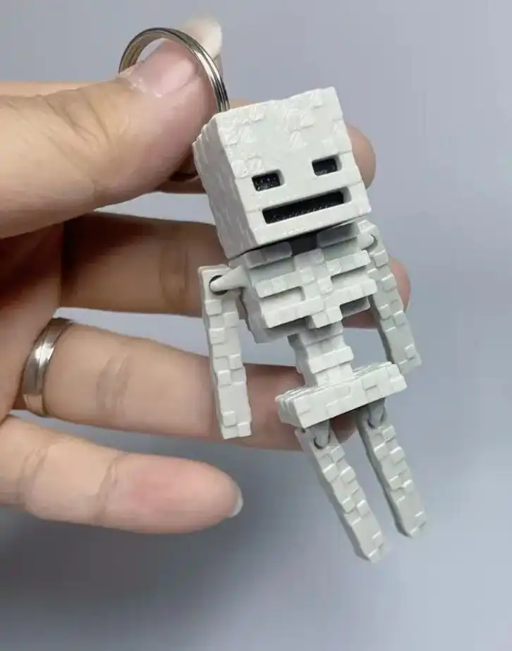 _ 1 Close-up of a person holding a blocky, articulated skeleton keychain resembling a Minecraft character against a neutral background. | Sky Rye Design Close-up of a person holding a blocky, articulated skeleton keychain resembling a Minecraft character against a neutral background.