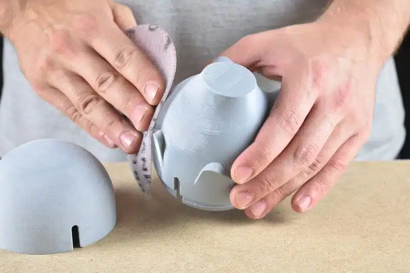 Hands sanding a 3D printed object for a smooth finish, demonstrating post-processing techniques in 3D printing.
