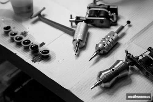 _ 10 Black and white photo of tattoo equipment on a table, featuring tattoo machines and ink cups for professional artistry. | Sky Rye Design Black and white photo of tattoo equipment on a table, featuring tattoo machines and ink cups for professional artistry.