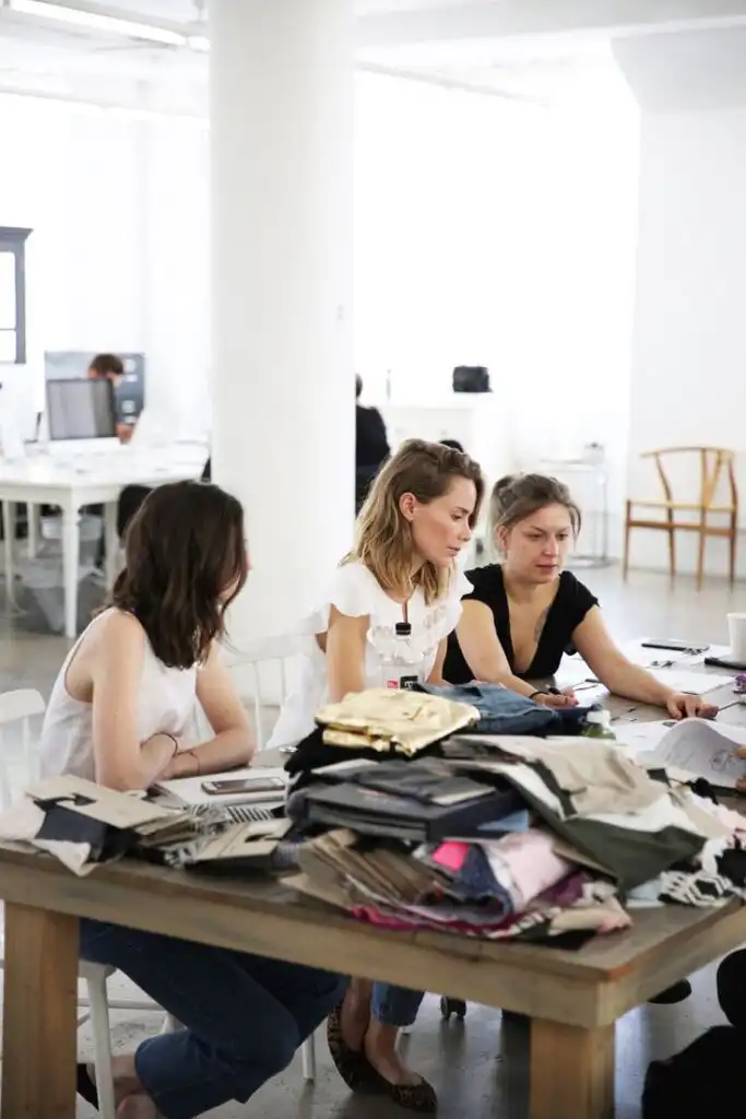 Fashion designers collaborate on a project, surrounded by fabric samples, in a modern, bright workspace.
