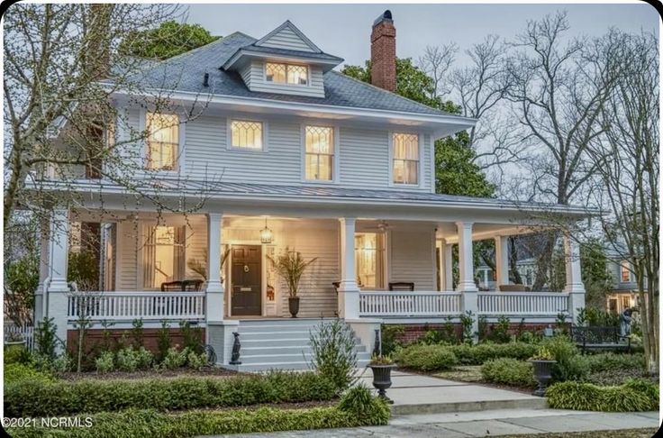 _ 11 Charming two-story classic house with wraparound porch, warm lights, and lush greenery at dusk. | Sky Rye Design Charming two-story classic house with wraparound porch, warm lights, and lush greenery at dusk.