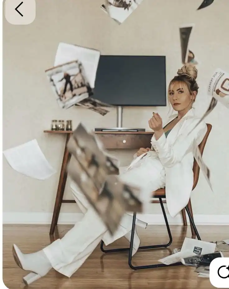 _ 11 Woman in white suit sits confidently amidst floating papers in modern living room, stylishly blending chaos and elegance. | Sky Rye Design Woman in white suit sits confidently amidst floating papers in modern living room, stylishly blending chaos and elegance.
