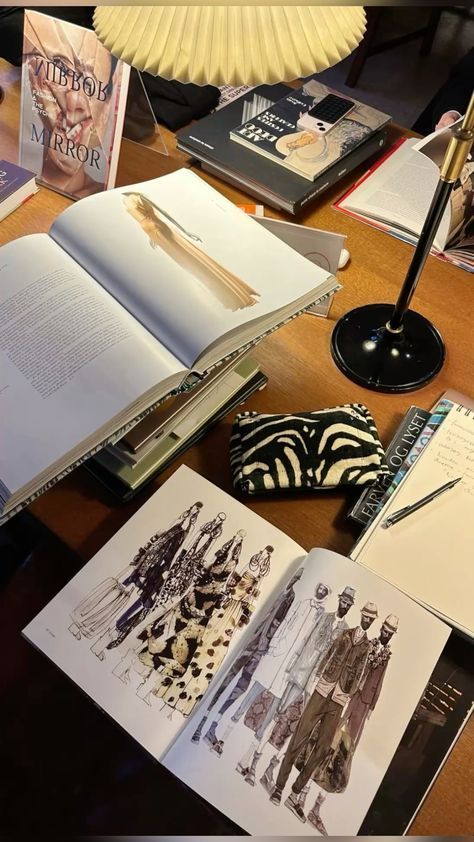 _ 11 Open fashion sketchbooks on a wooden desk surrounded by books, a zebra-patterned pouch, and a lamp. Ideal for design inspiration. | Sky Rye Design Open fashion sketchbooks on a wooden desk surrounded by books, a zebra-patterned pouch, and a lamp. Ideal for design inspiration.