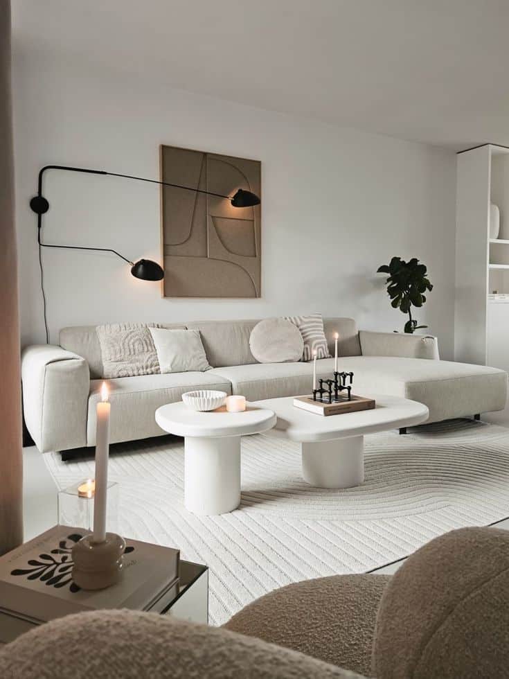 Modern living room with white sectional sofa, abstract wall art, coffee tables, neutral decor, and soft lighting for a cozy ambiance.