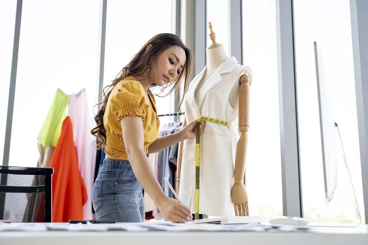 Fashion designer measuring dress on mannequin in bright studio, focusing on precision.