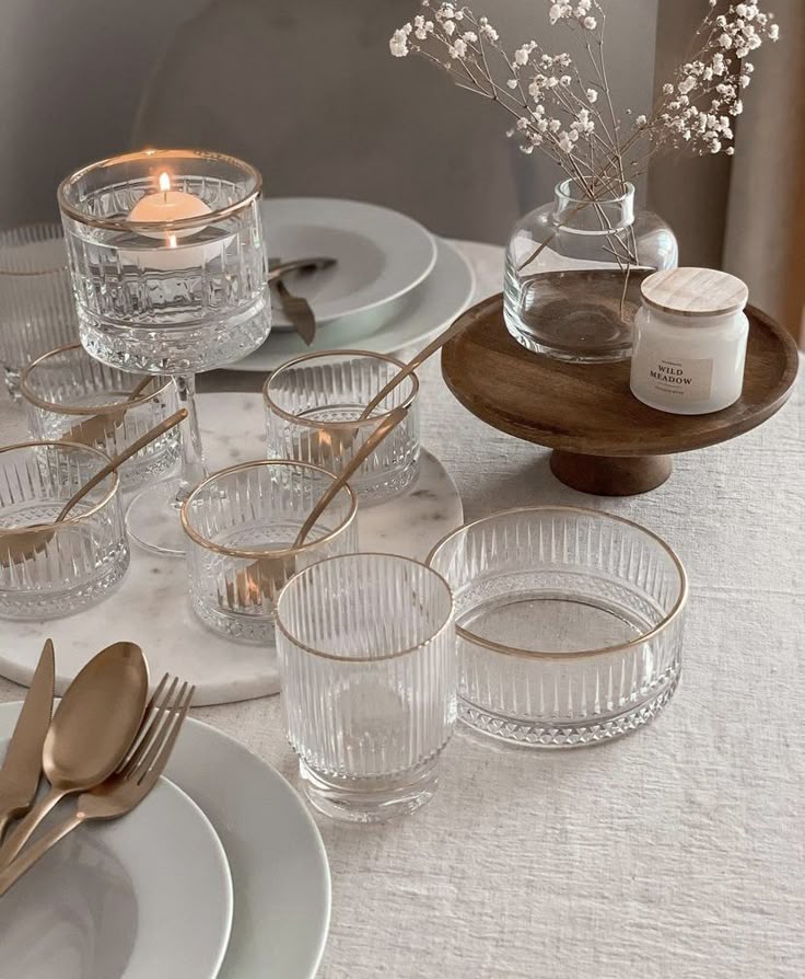 _ 12 Elegant table setting with glassware, gold cutlery, a lit candle, and minimalist decor on a white tablecloth, creating a serene dining ambiance. | Sky Rye Design Elegant table setting with glassware, gold cutlery, a lit candle, and minimalist decor on a white tablecloth, creating a serene dining ambiance.