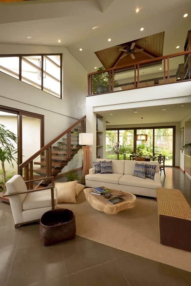 _ 12 Modern living room with high ceilings, cozy seating, wooden staircase, and large windows showcasing a lush garden view. | Sky Rye Design Modern living room with high ceilings, cozy seating, wooden staircase, and large windows showcasing a lush garden view.