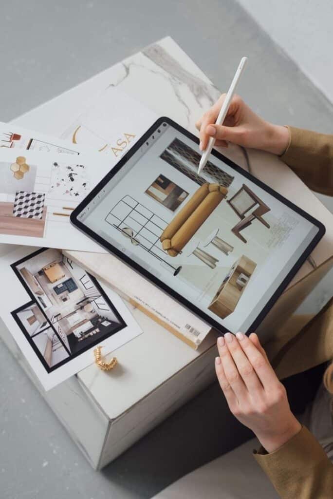 Designer using a tablet with a stylus to create an interior design plan, surrounded by mood boards and design sketches.