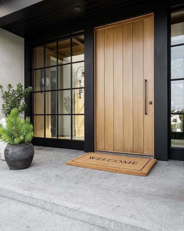 _ 12 Modern wooden front door with black frame, glass panels, and a welcome mat on stone steps, next to a potted plant. | Sky Rye Design Modern wooden front door with black frame, glass panels, and a welcome mat on stone steps, next to a potted plant.