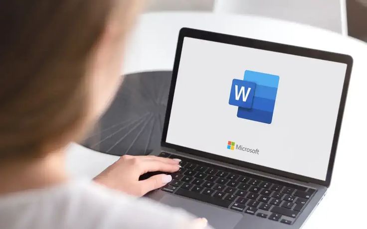 12 Useful Microsoft Word Tips and Tricks Person using a laptop displaying Microsoft Word logo, emphasizing digital document creation and editing. | Sky Rye Design Person using a laptop displaying Microsoft Word logo, emphasizing digital document creation and editing.