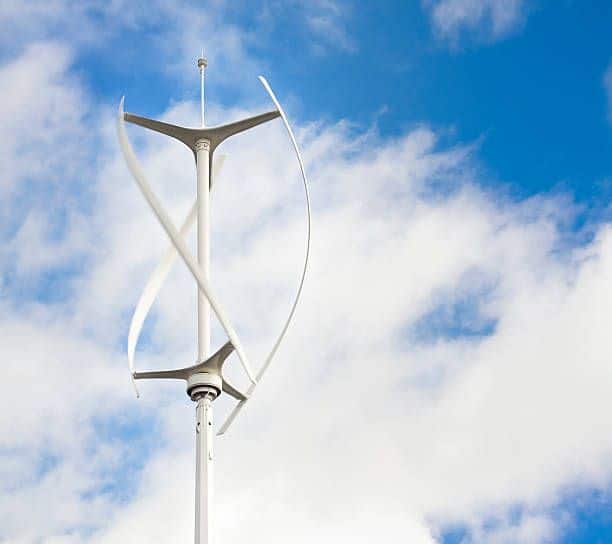 Vertical axis wind turbine against a clear blue sky with clouds, showcasing renewable energy technology and sustainable power solutions.
