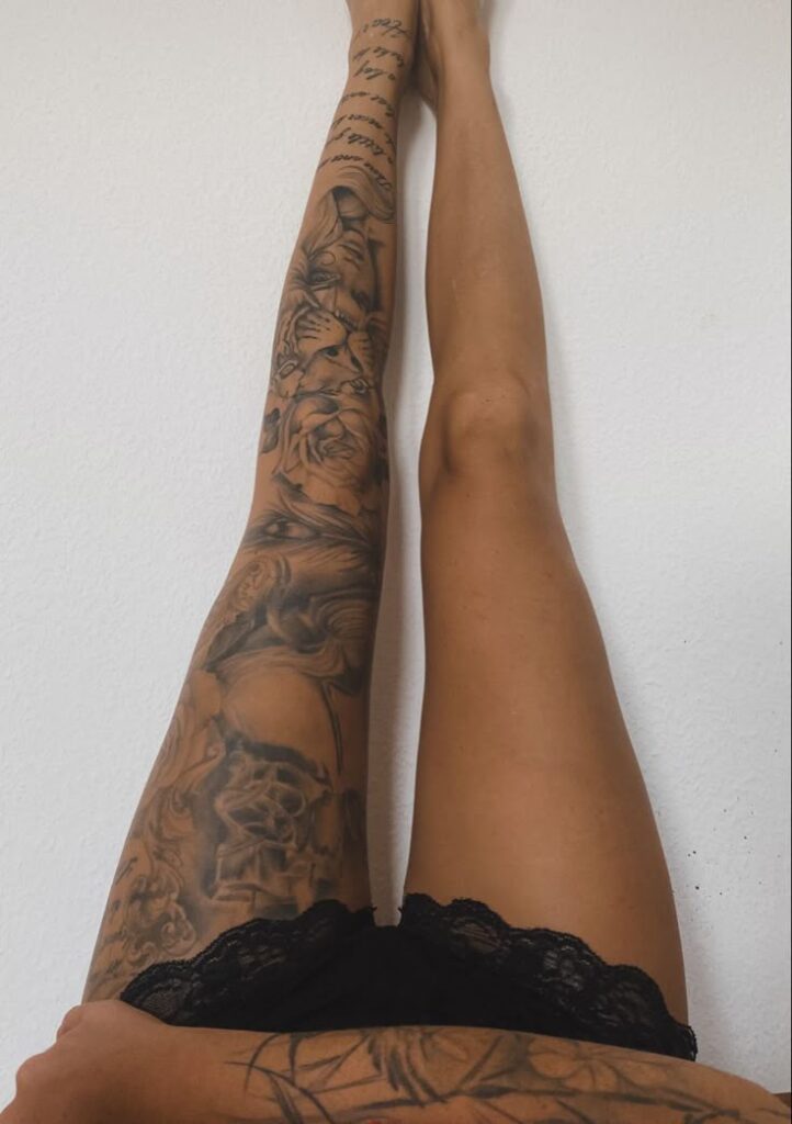 _ 13 Two legs against a white wall, one adorned with detailed tattoos, the other bare, wearing black lace shorts. | Sky Rye Design Two legs against a white wall, one adorned with detailed tattoos, the other bare, wearing black lace shorts.