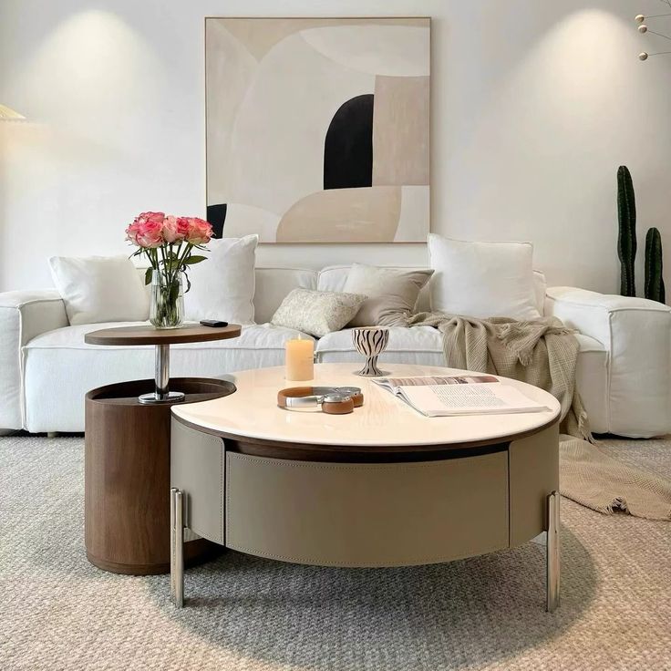 _ 14 Modern living room with white sofa, abstract artwork, and round coffee table with flowers, candle, and book. Cozy and stylish decor. | Sky Rye Design Modern living room with white sofa, abstract artwork, and round coffee table with flowers, candle, and book. Cozy and stylish decor.