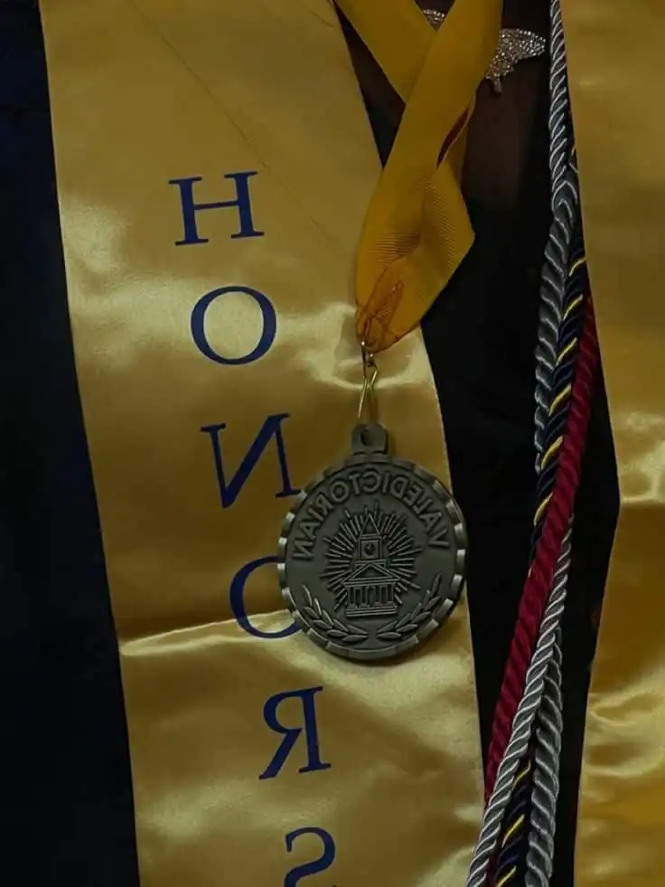 Graduation attire featuring a gold honor stole, valedictorian medal, and multi-colored cords, symbolizing academic excellence and achievement.
