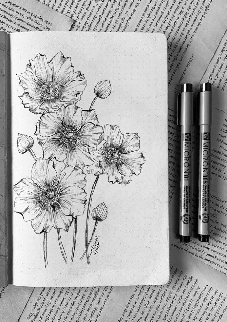 Sketch of blooming flowers in a notebook, accompanied by two Micron pens, resting on printed pages. Ideal for art and drawing themes.