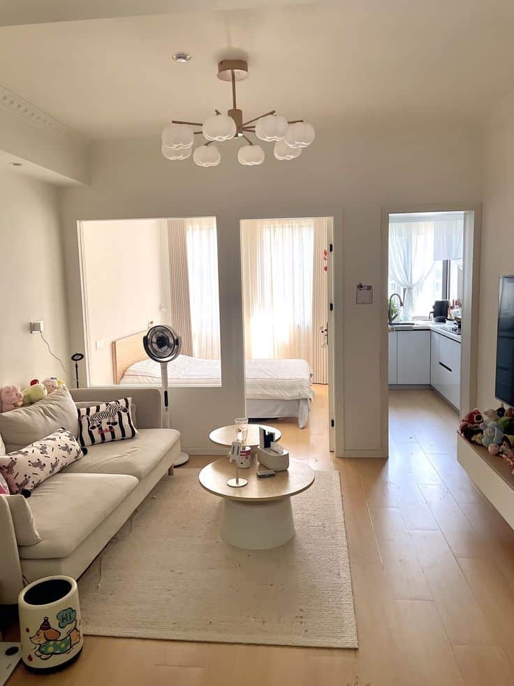 _ 18 Modern open-plan living room with cozy sofa, coffee table, and view into bedroom and kitchen. Stylish lighting and bright decor. | Sky Rye Design Modern open-plan living room with cozy sofa, coffee table, and view into bedroom and kitchen. Stylish lighting and bright decor.