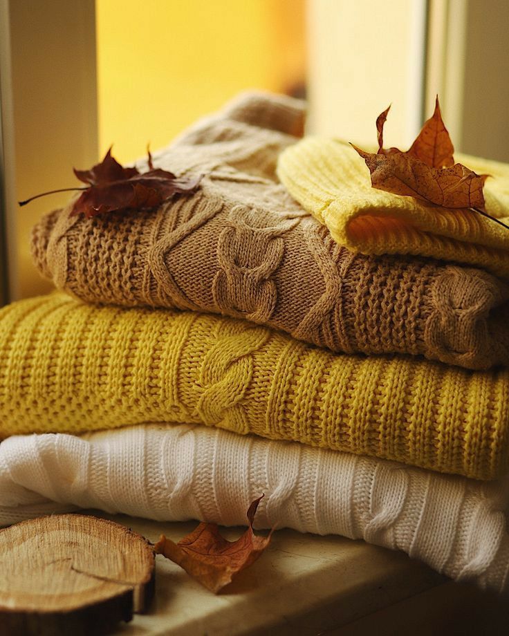 _ 18 Cozy autumn sweaters stacked by a window with fall leaves, showcasing warm knit textures in beige, mustard, and white hues. | Sky Rye Design Cozy autumn sweaters stacked by a window with fall leaves, showcasing warm knit textures in beige, mustard, and white hues.