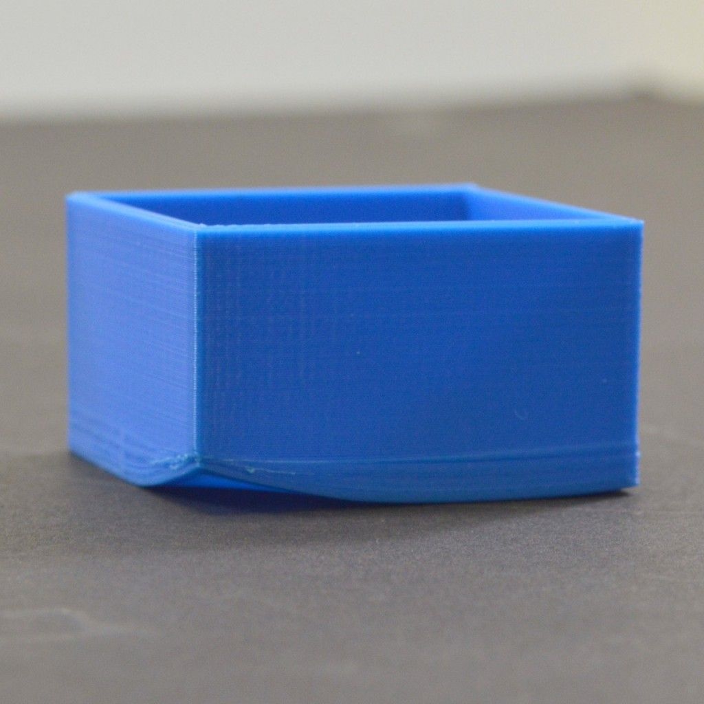 Blue 3D printed cube on gray surface, showcasing low-quality print layers and imperfections for 3D printing analysis.