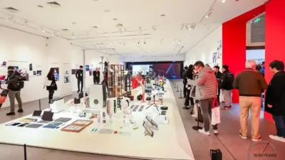 People explore a modern exhibition showcasing various gadgets and tech innovations, highlighted by bright lighting and informative displays.