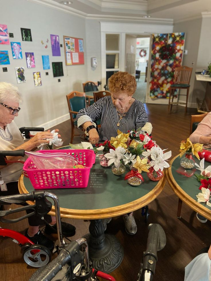 Older adults crafting holiday decorations at a table, surrounded by colorful festive materials in a cozy community room.
