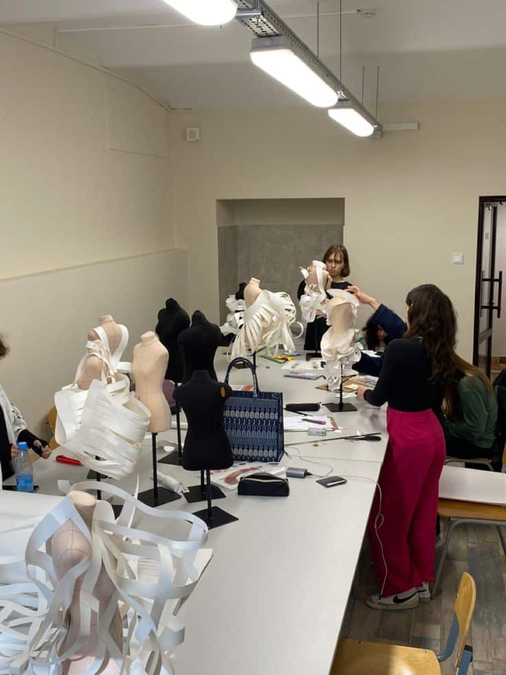 _ 2 Fashion design students work on dress forms with paper details in a classroom, showcasing creativity and collaboration in garment creation. | Sky Rye Design Fashion design students work on dress forms with paper details in a classroom, showcasing creativity and collaboration in garment creation.