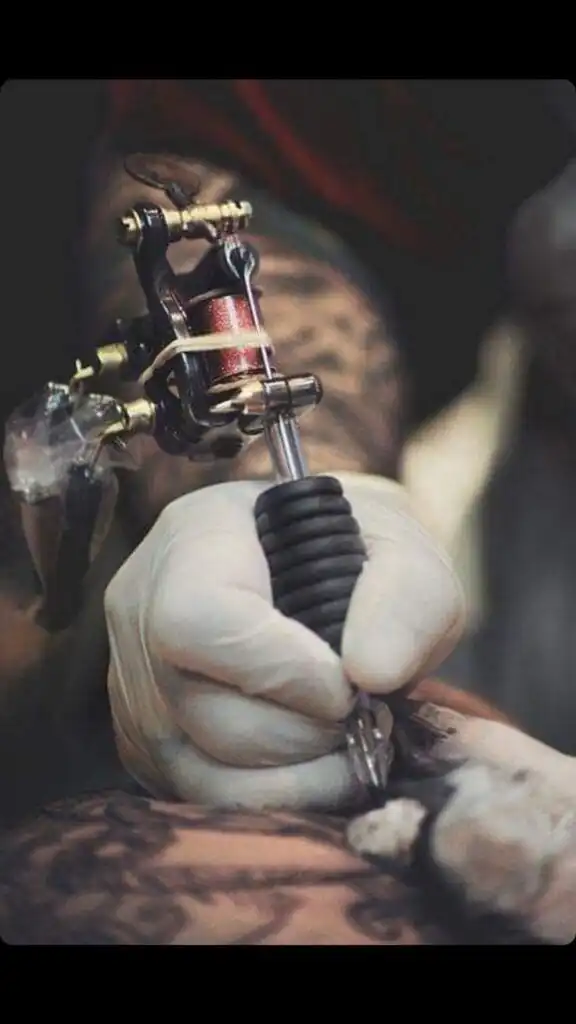 Tattoo artist with gloved hand using a tattoo machine to ink intricate design on skin. Close-up of tattooing process and tools.