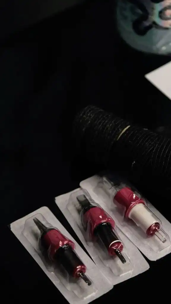 Tattoo needles in blister packs on a table, alongside coiled black wrap, ready for use in tattooing or piercing sessions.