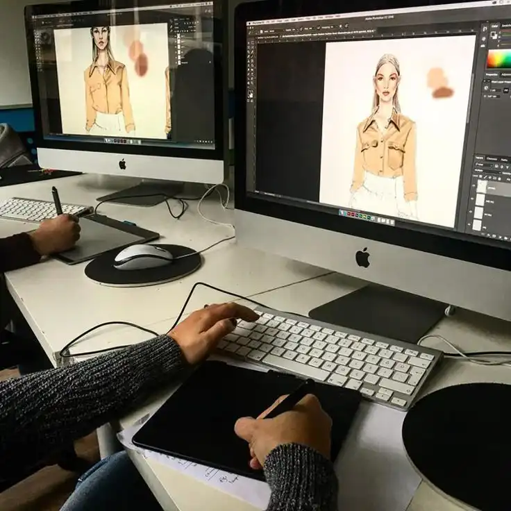 Designer using a graphics tablet and software on an iMac to create digital fashion illustrations in a studio setting.