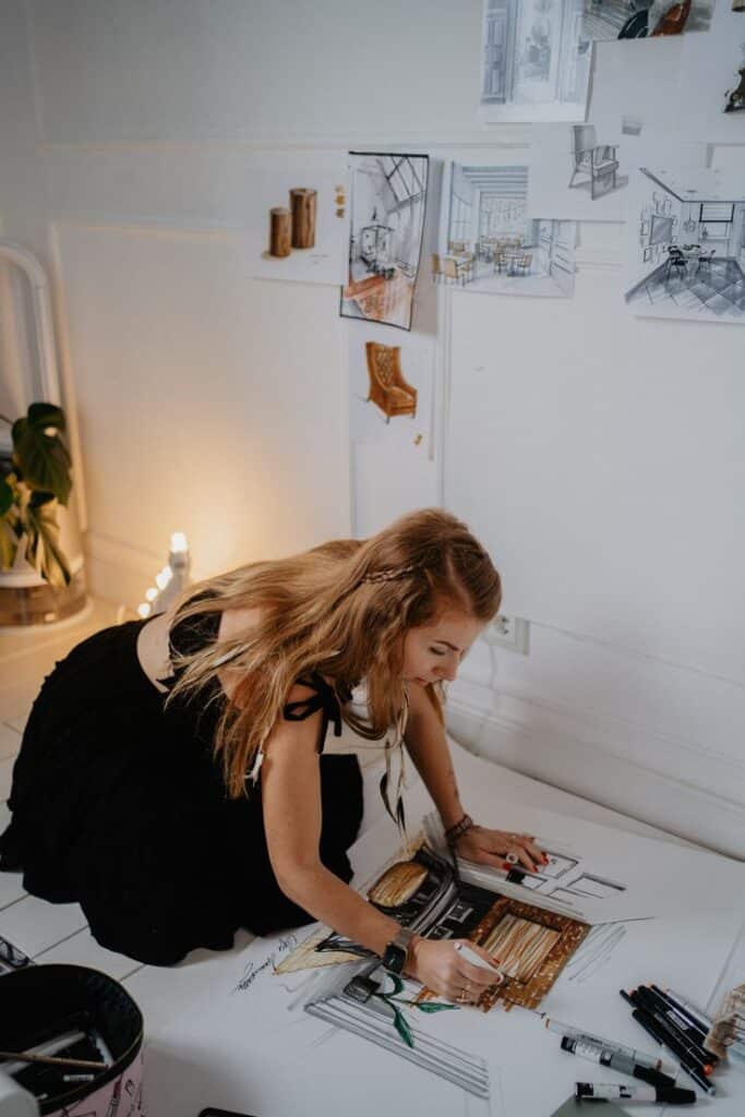 Artist sketching interior design ideas on the floor, surrounded by concept art and creative tools in a bright studio.