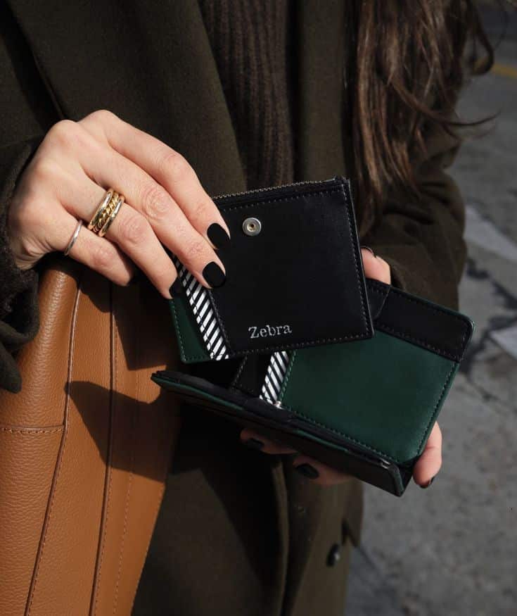 Person holding a stylish black and green wallet in outdoor setting, featuring a striped interior and Zebra branding.