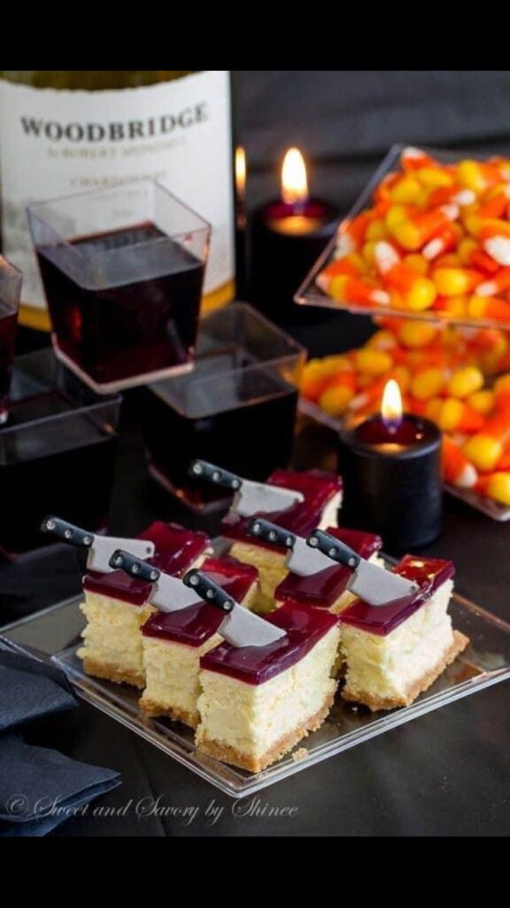 Screenshot Halloween-themed cheesecake bites with knife toppers, surrounded by wine, candy corn, and candles on a festive black table. | Sky Rye Design Halloween-themed cheesecake bites with knife toppers, surrounded by wine, candy corn, and candles on a festive black table.