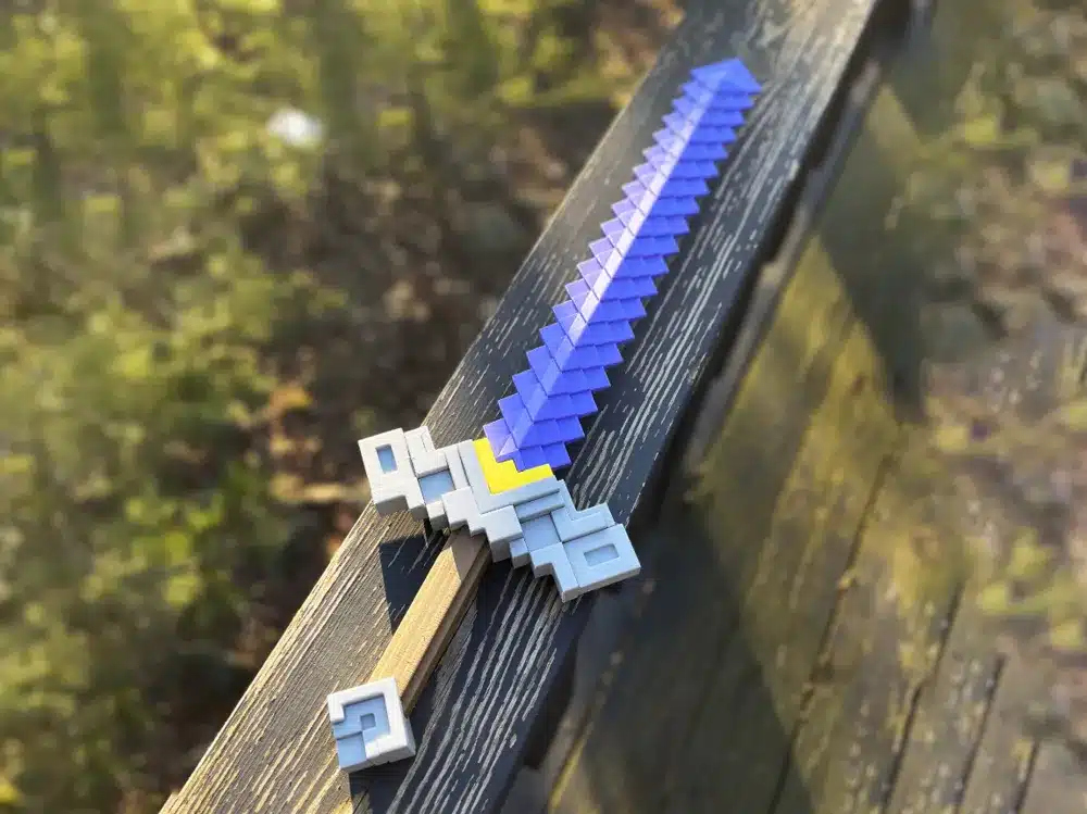 2025-04-29_226e43423fbee Pixelated purple and grey sword on a wooden railing, inspired by block-style video games, with a blurred forest background. | Sky Rye Design Pixelated purple and grey sword on a wooden railing, inspired by block-style video games, with a blurred forest background.