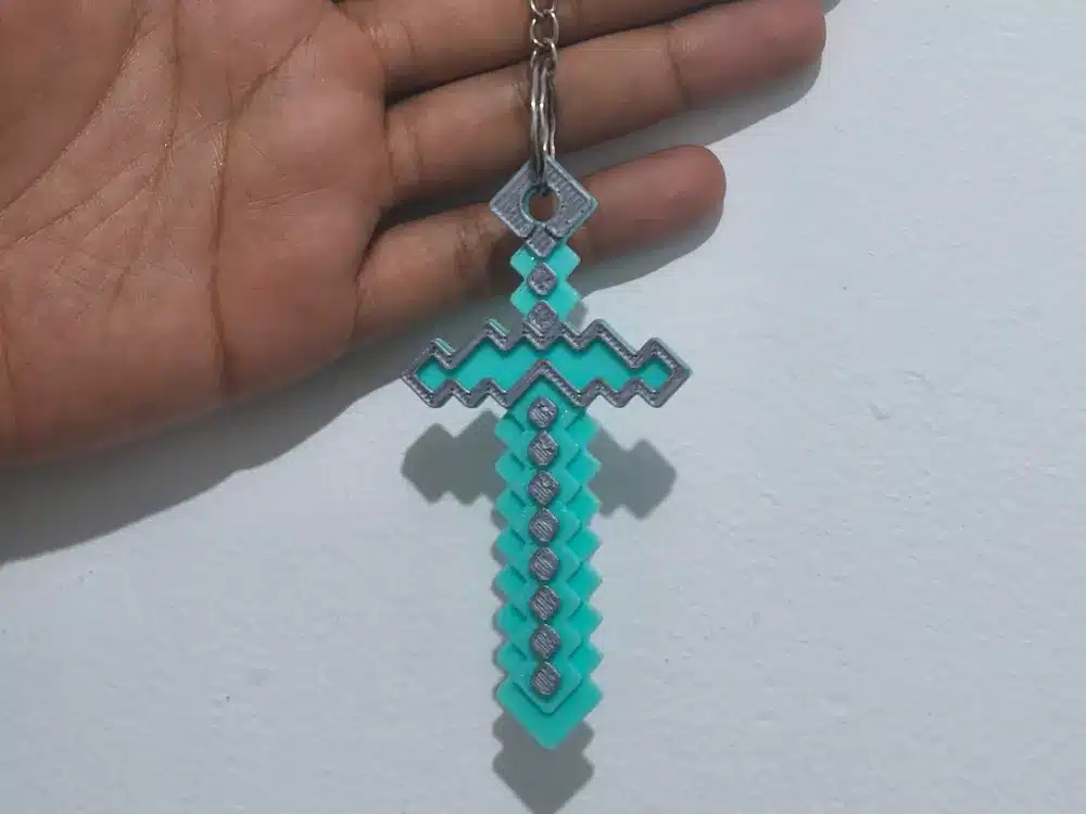 2025-05-03_5c926c407db75 Person holding a pixelated blue sword keychain inspired by a video game, on a white background. | Sky Rye Design Person holding a pixelated blue sword keychain inspired by a video game, on a white background.