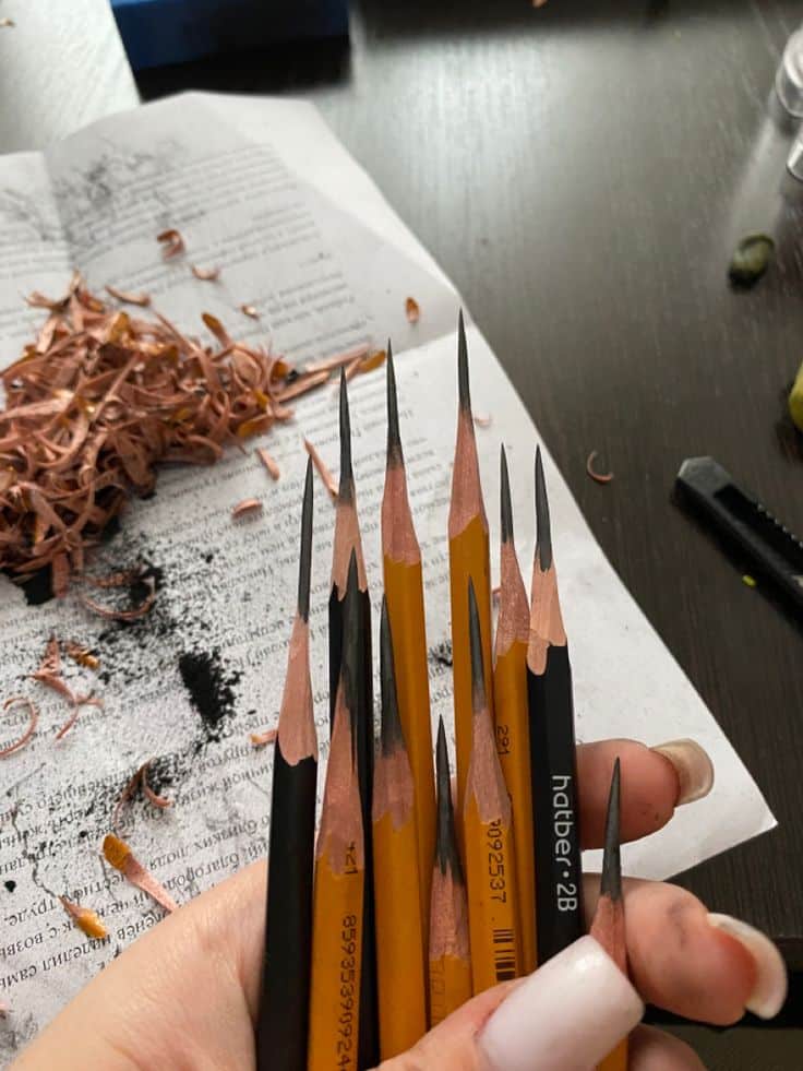 Sharpened pencils held in hand over a page, surrounded by shavings and smudges, ready for sketching or writing.