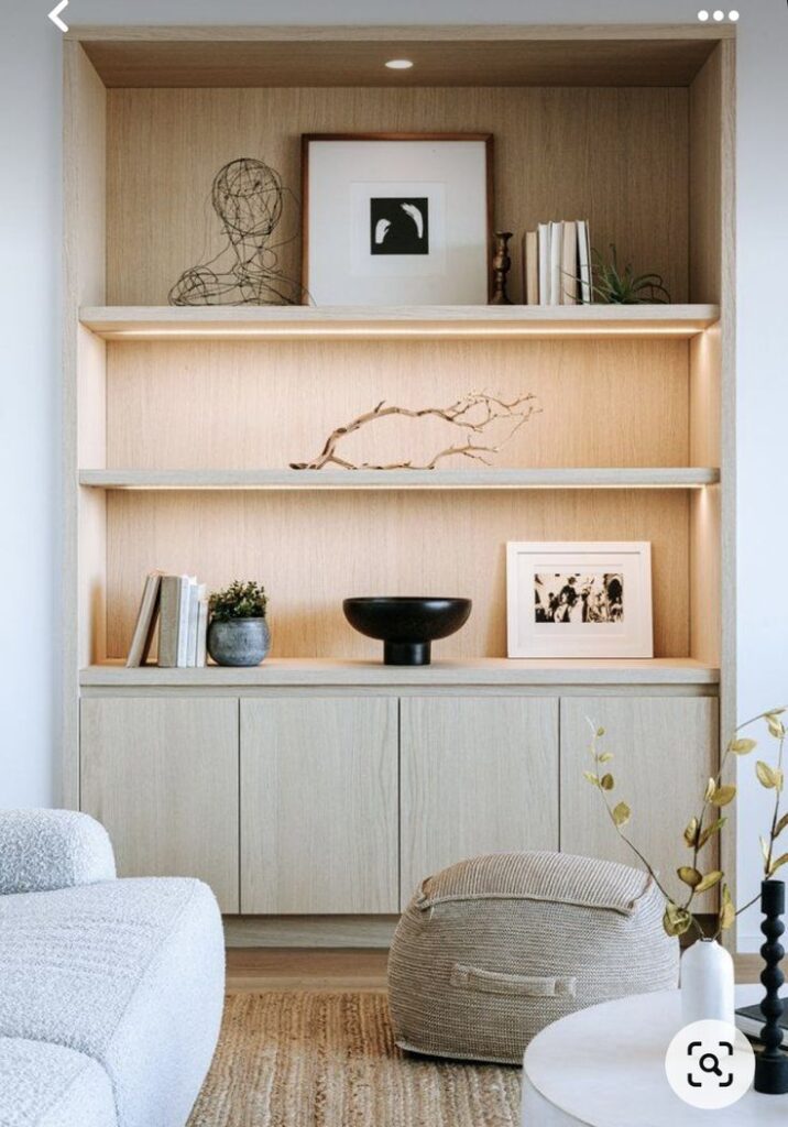 _ - 2025-12-01T200811018 Minimalist wooden shelf with art, books, plants, and decor in a cozy, modern living room setting featuring a pouf and textured rug. | Sky Rye Design Minimalist wooden shelf with art, books, plants, and decor in a cozy, modern living room setting featuring a pouf and textured rug.