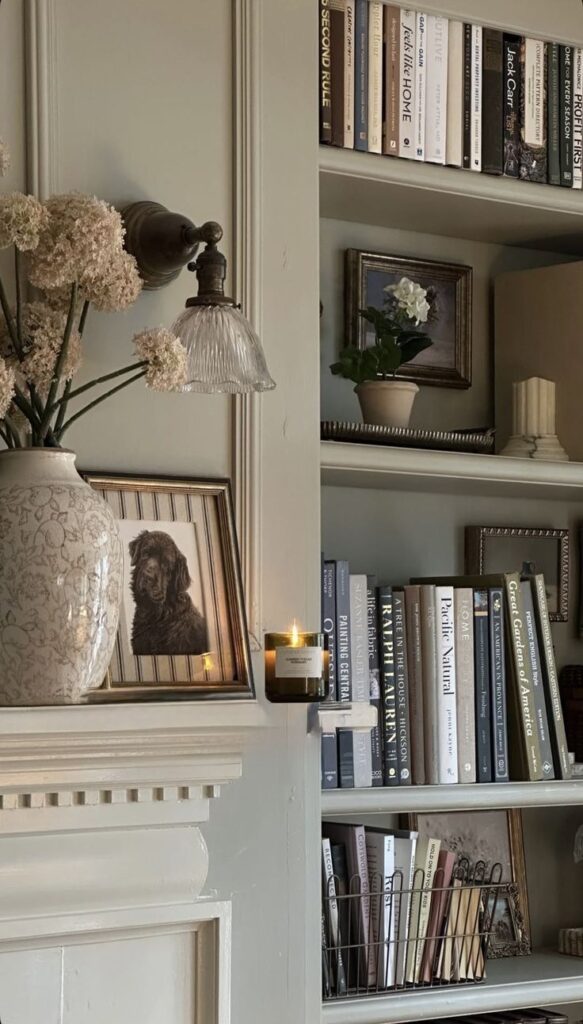 _ - 2025-12-01T203437114 Cozy interior with a bookshelf, framed dog portrait, soft lighting, and a candle on a mantel, creating a warm, inviting ambiance. | Sky Rye Design Cozy interior with a bookshelf, framed dog portrait, soft lighting, and a candle on a mantel, creating a warm, inviting ambiance.