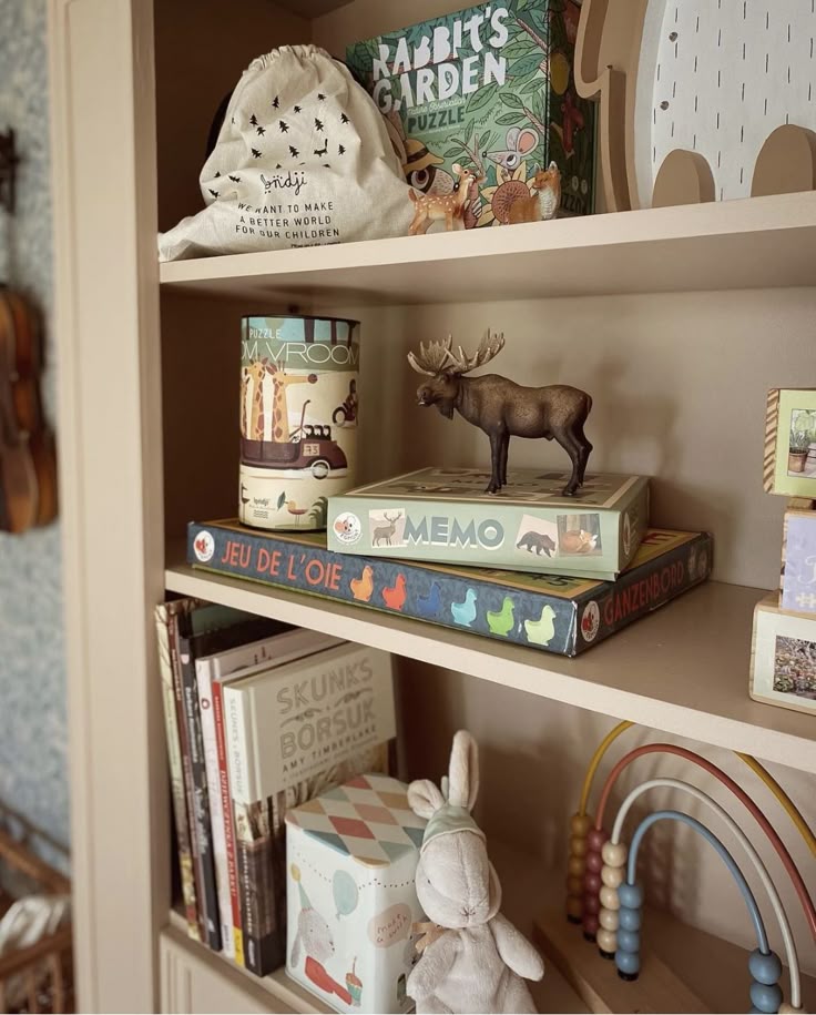 _ - 2025-12-01T204743842 Children's bookshelf with puzzles, books, a toy moose, rainbow beads, and a stuffed bunny. Cozy playroom decor for kids. | Sky Rye Design Children's bookshelf with puzzles, books, a toy moose, rainbow beads, and a stuffed bunny. Cozy playroom decor for kids.