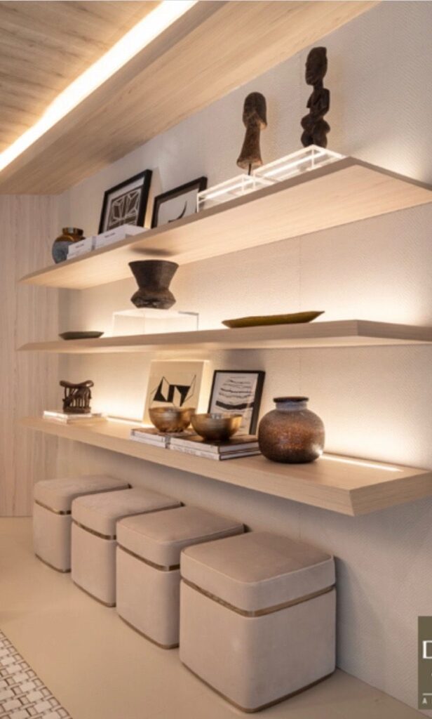 _ - 2025-12-01T211443645 Modern shelf display with wooden sculptures, pottery, framed art, and books. Minimalist decor with soft lighting and beige ottomans below. | Sky Rye Design Modern shelf display with wooden sculptures, pottery, framed art, and books. Minimalist decor with soft lighting and beige ottomans below.