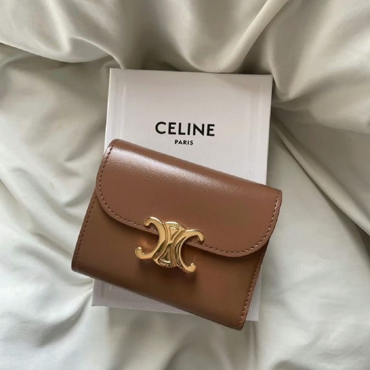 Brown Celine wallet with a gold logo on a white Celine Paris box, resting on a soft fabric background. Aesthetic Wallets
